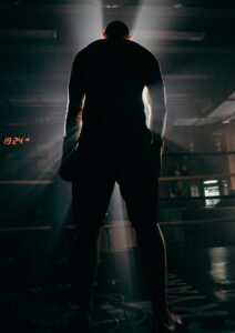 Silhouette of a boxer in a gym, illuminated by dramatic beams of sunlight, creating a powerful visual impact.