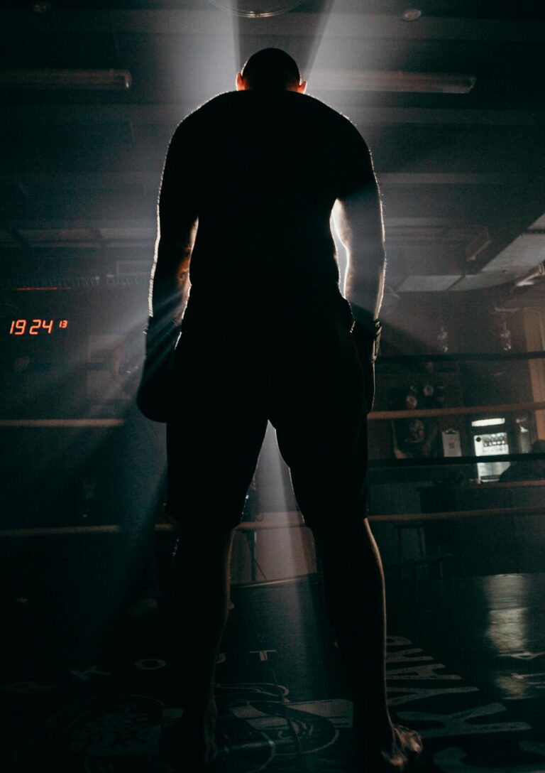 Silhouette of a boxer in a gym, illuminated by dramatic beams of sunlight, creating a powerful visual impact.