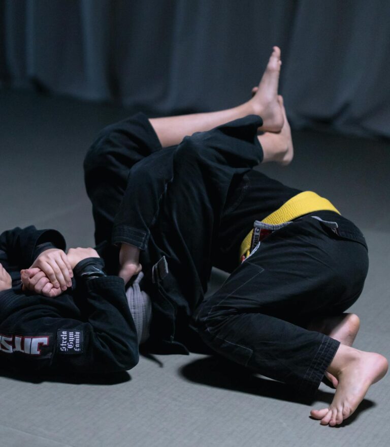 Two boys engaged in a jiu jitsu sparring session on an indoor mat, showcasing martial arts skills.